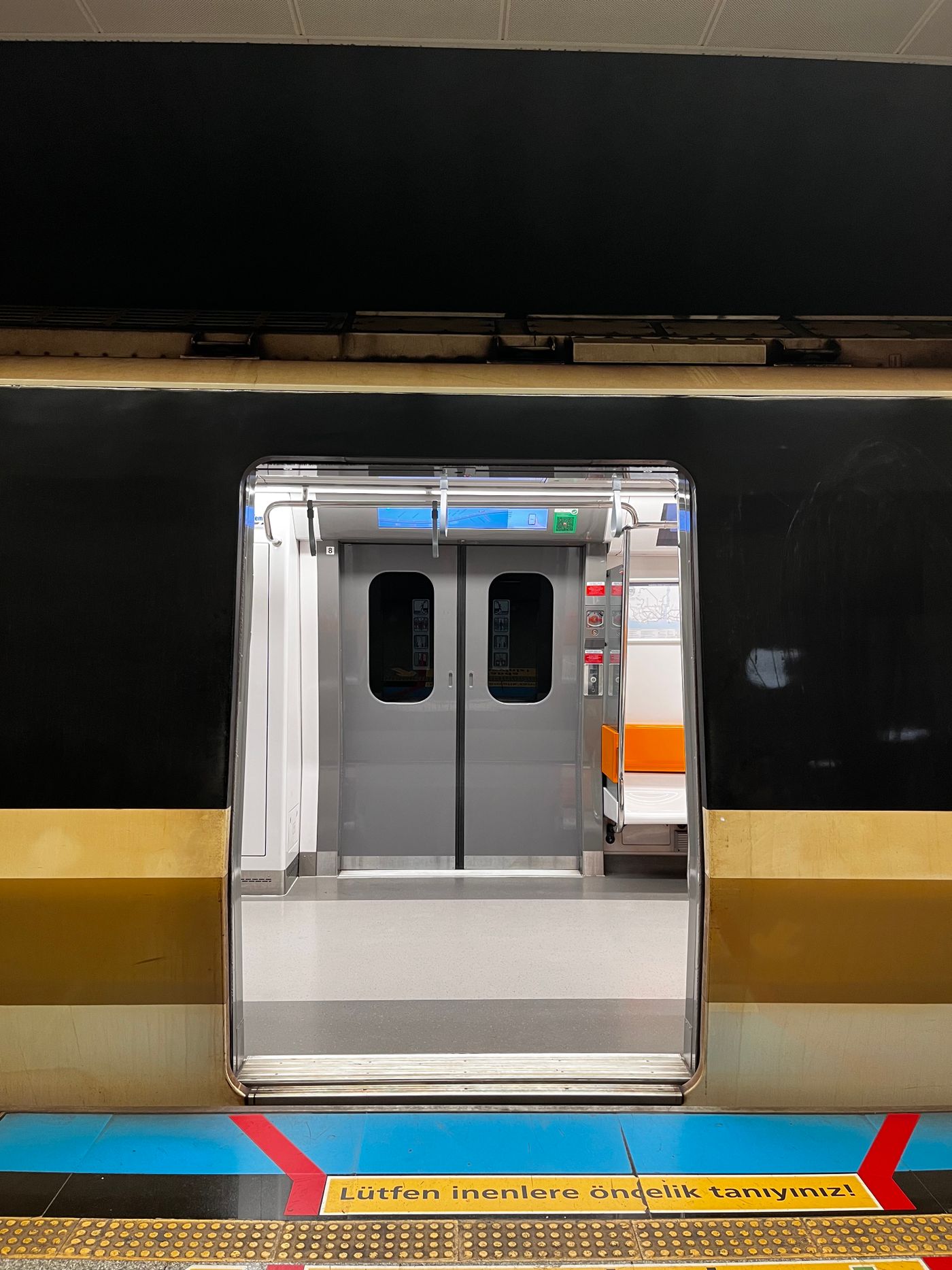 Open doors of a modern Istanbul metro train at a station platform with a Turkish priority sign