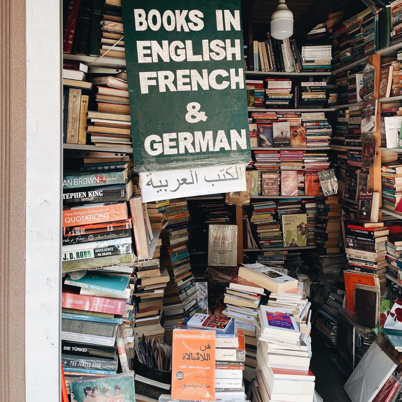 A crammed second-hand bookshop with a sign reading Books in English French and German over floor-to-ceiling stacks