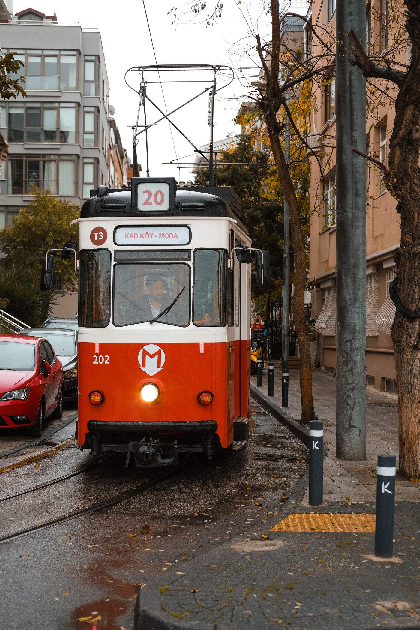 A vintage Kadıköy–Moda heritage tram, route 20, working its way down a wet Moda street past parked cars and apartment blocks